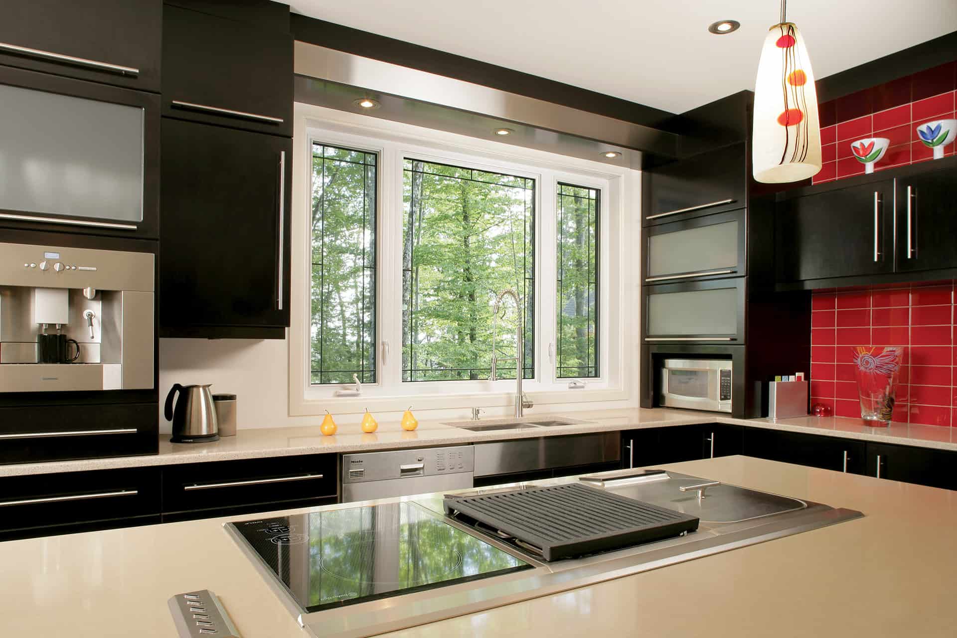 a modern kitchen with black cabinets, red tile and large window behind the sink.